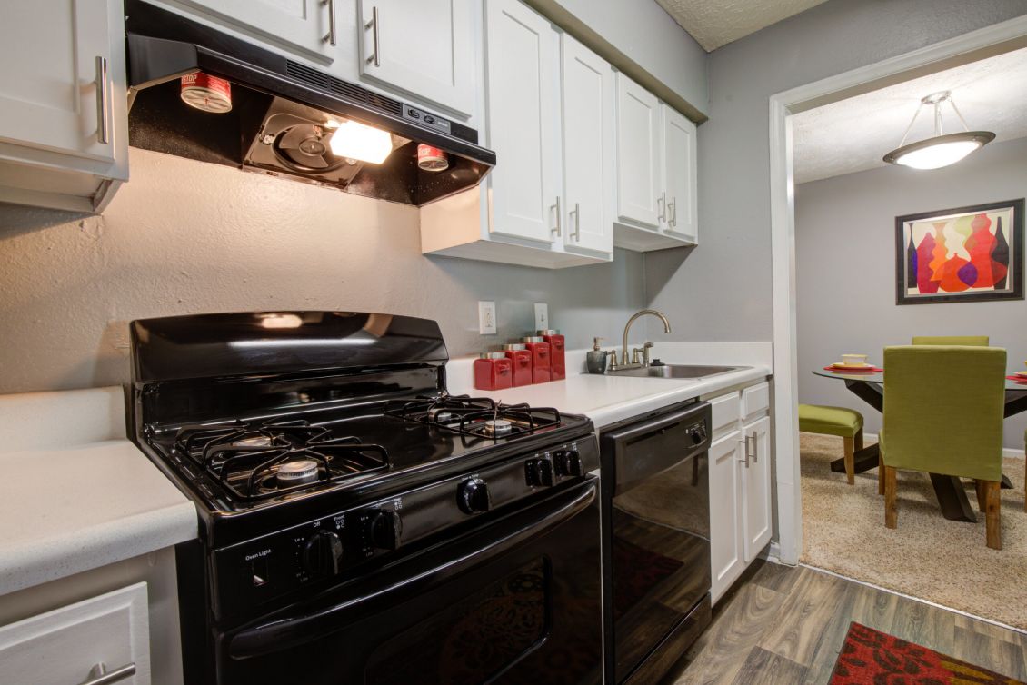 Modern kitchen with black stove and oven, white cabinets, and view into a dining room with green chairs.
