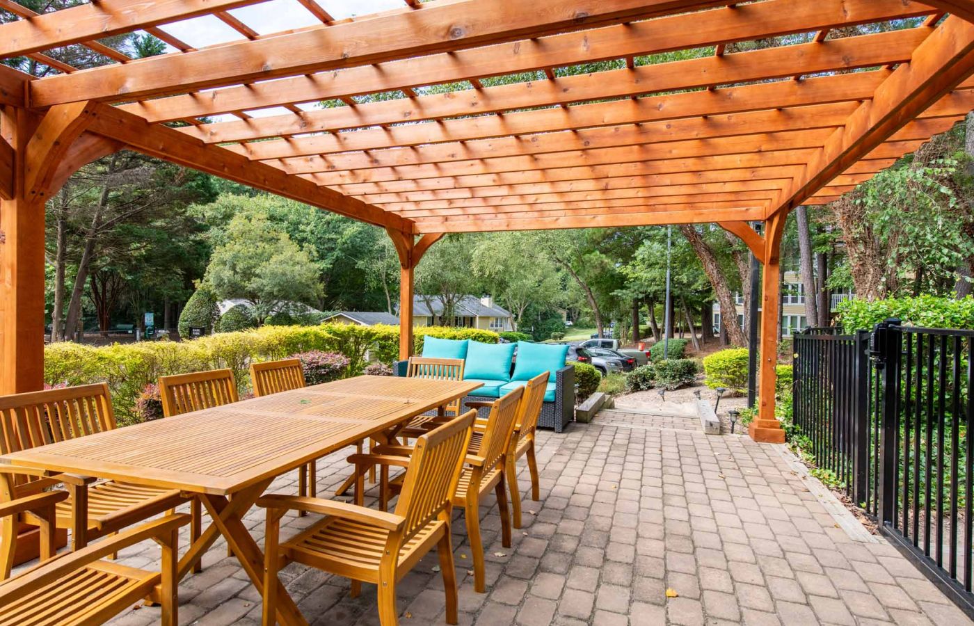 Wooden pergola over outdoor dining set with cushions on a brick patio, surrounded by greenery.