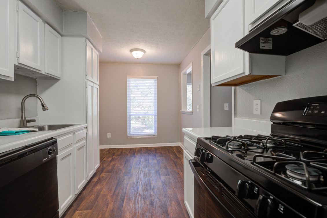 Modern kitchen with white cabinets, gas stove, dishwasher, and window letting in natural light.