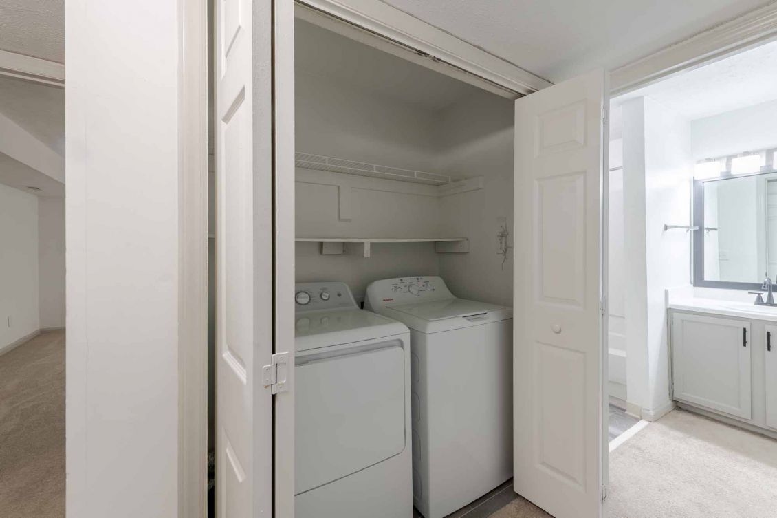 Laundry closet with a washer and dryer next to a bathroom with a sink and mirror.