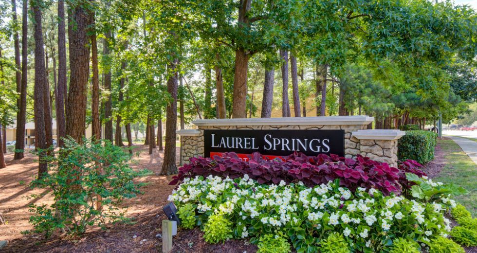 Stone sign for Laurel Springs, surrounded by colorful flowers and trees along a landscaped path.