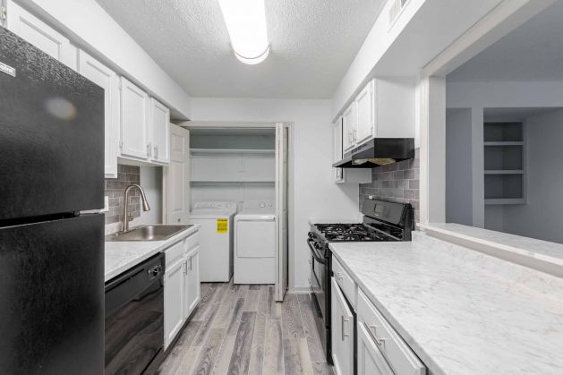 Modern kitchen with white cabinets, black appliances, marble countertops, and a laundry area in the back.