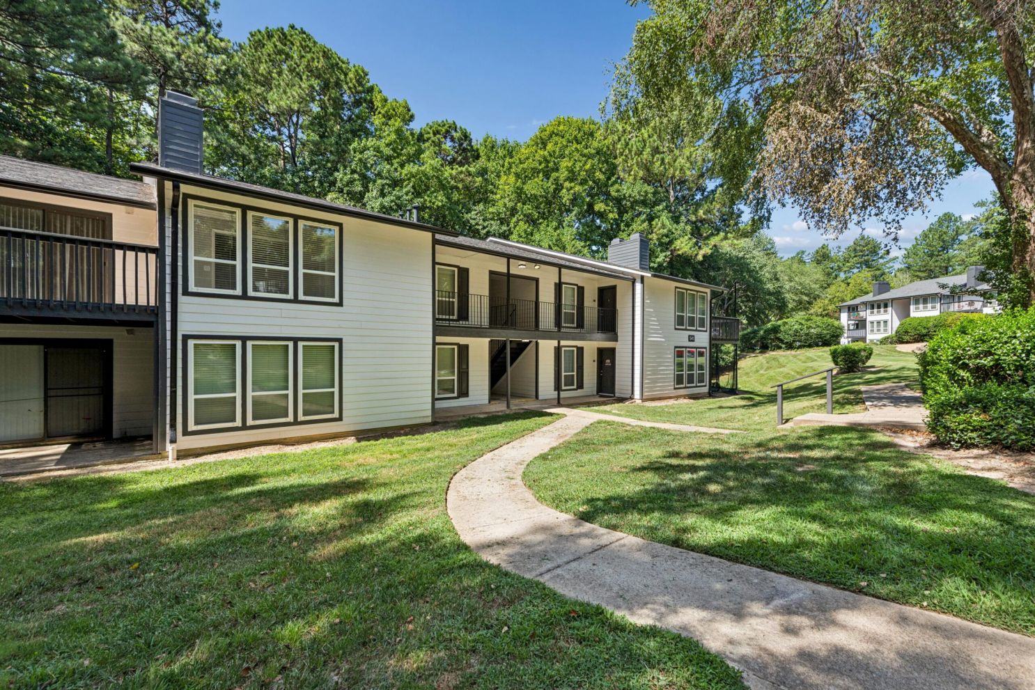 Two-story apartment building with white siding and black trim, surrounded by a grassy lawn and a concrete walkway.